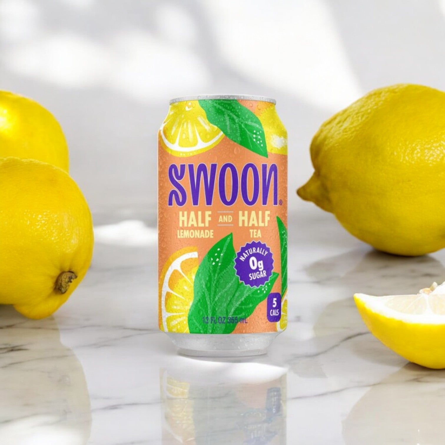 A can of Swoon Half & Half Black Tea and Lemonade, monk fruit sweetened with "0g sugar" and "5 calories," is surrounded by whole and halved lemons on a marble surface.