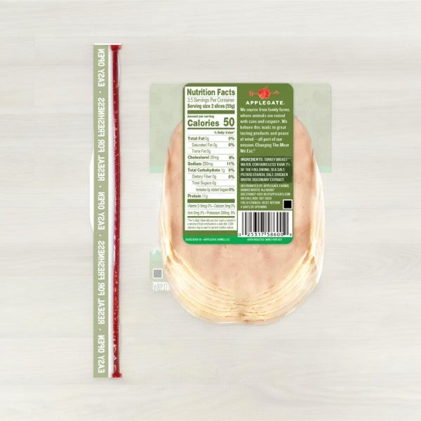 A sealed package of Applegate Natural Sliced Oven Roasted Turkey Breast, 7 oz - 1 Count, Whole30 Approved and antibiotic-free, lies flat on a light wooden surface. A measuring stick is placed parallel to the left side, showing a length of approximately 10 inches.
