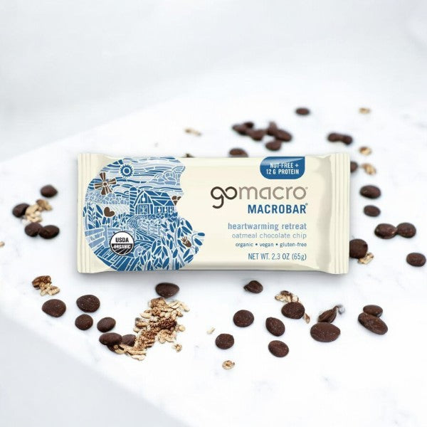 The GoMacro Oatmeal Chocolate Chip MacroBar (2.3 oz, 1 count) from the brand GoMacro, showcased on a marble surface and surrounded by scattered oats and chocolate chips, highlights its organic, plant-based goodness.