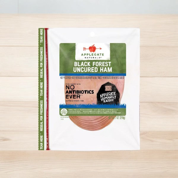 A package of Applegate Natural Uncured Black Forest Ham, 7 oz-1 Count, featuring antibiotic-free pork, is placed on a wooden surface. The packaging highlights "No Antibiotics Ever" and "Applegate Humanely Raised," ensuring high-quality, gluten-free ham for your meals.