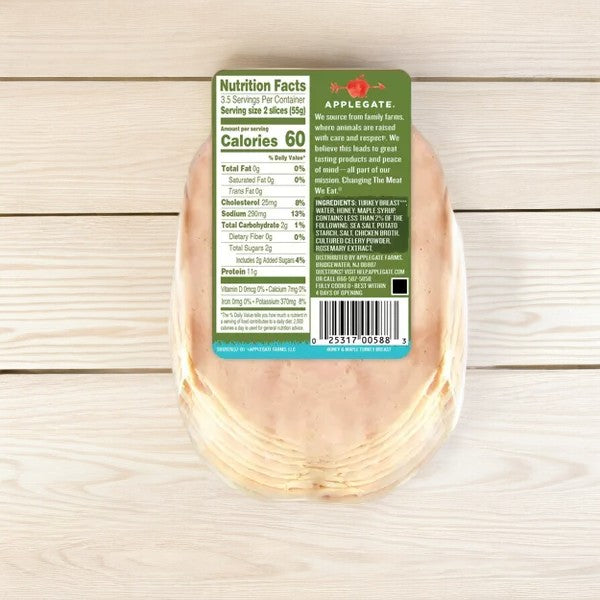 A 7 oz package of Applegate Natural Honey & Maple Turkey Breast on a wooden surface, displaying nutritional facts, ingredient list, and barcode. The label emphasizes that it’s made from humanely raised turkeys with natural ingredients.