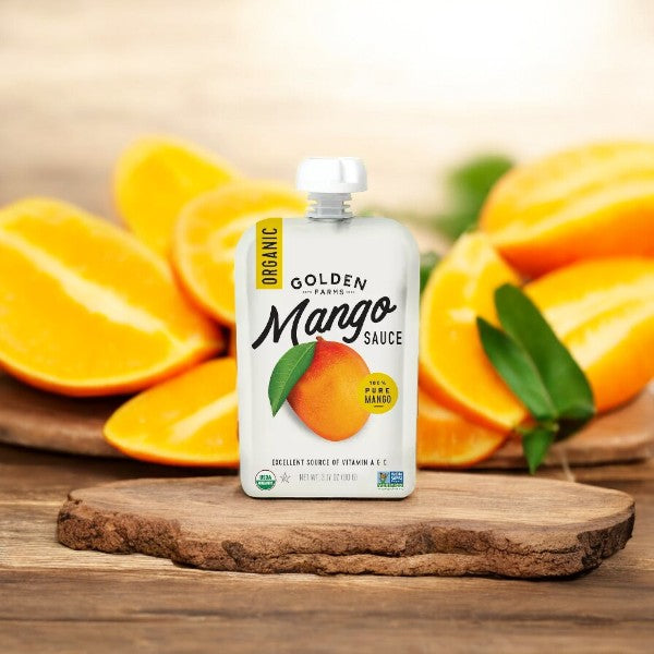 A pouch of Golden Farms Organic Mango Squeeze (3.17oz, 1 count) from Golden Farms is placed on a wooden slab with sliced mangoes in the background, brimming with Vitamin C.