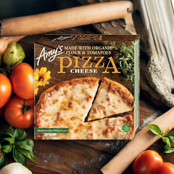 An Amy's Cheese Frozen Pizza-1 Count in its box is displayed among fresh ingredients like tomatoes, basil, and flour, emphasizing its organic flour and tomatoes.