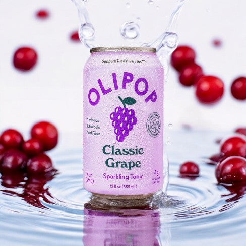 A single 12 fl oz can of Olipop Classic Grape sparkling tonic, featuring non-GMO ingredients and infused with probiotics and prebiotics for digestive health, surrounded by red berries in water.