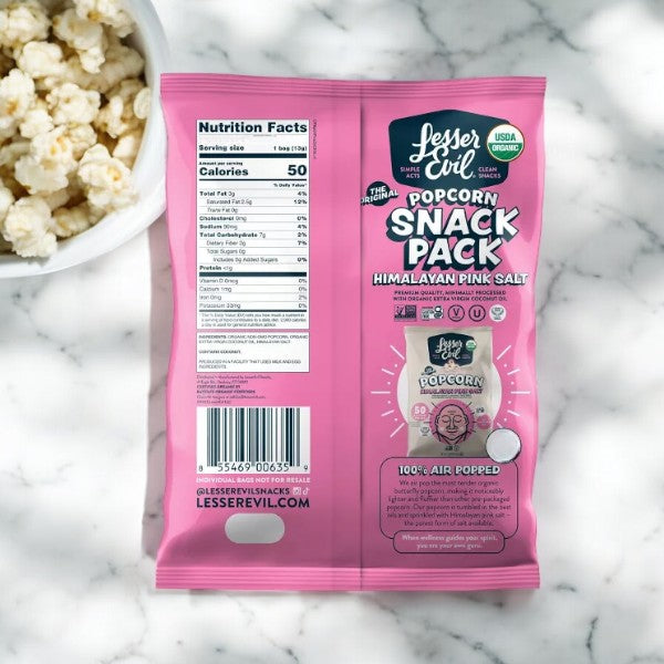 A bag of LesserEvil Organic Popcorn, Snack Pack, Himalayan Pink flavor (0.46 oz), a healthy snack displayed on a marble surface. The pink and white packaging highlights its gluten-free quality, with nutrition facts and product information visible.