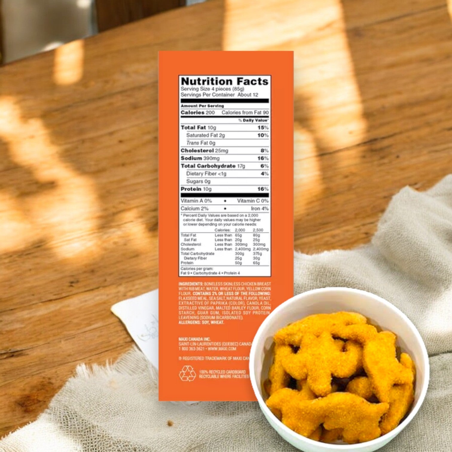 A nutrition facts label on an orange background with a bowl of Yummy Dino Buddies Chicken Nuggets 67 oz by Yummy, made from white meat chicken and rich in omega-3 fatty acids, placed on a cloth in the foreground.