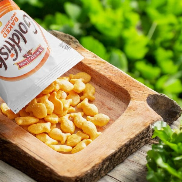 A bag of Pepperidge Farm Goldfish Cheddar Crackers 1.25 oz is partially emptied into a wooden bowl, showcasing the delicious cheddar flavor with greenery in the background. Perfect for convenient on-the-go snacking.