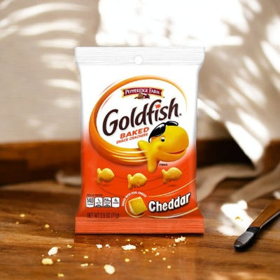 A 1.25 oz bag of Pepperidge Farm Goldfish Cheddar Crackers sits on a wooden surface with cracker crumbs around it, perfect for on-the-go snacking.