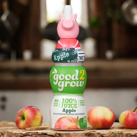 A 6 fluid ounce bottle of Easy Lunches Good2Grow Apple Juice, adorned with a collectible character top shaped like a pink pig, rests on a wooden surface surrounded by a few apples. Savor the wholesome goodness of 100% pure apple juice in every sip!