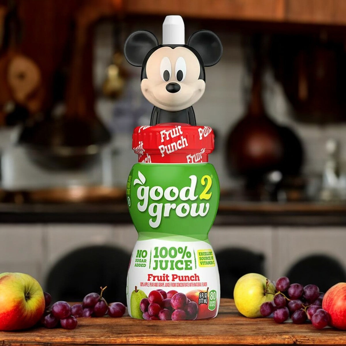 A 6 oz bottle of Good2grow Fruit Punch Juice from Easy Lunches, featuring a collectible character top with Mickey Mouse, surrounded by grapes on a kitchen counter.