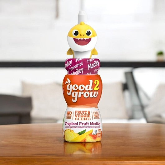 A 6 fl. oz. bottle of Easy Lunches Good2grow Single Serve Tropical Fruit Medley Juice, perfect for school lunches, featuring a yellow shark figurine topper, placed on a wooden table with a blurred background.