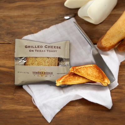 Timber Ridge Grilled Cheese on Texas Toast from Timber Ridge is displayed on a wooden surface, featuring a sliced sandwich, a napkin, and some unwrapped cheese sticks in the background.