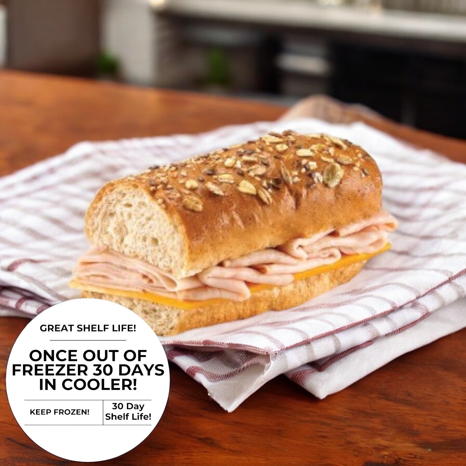 The E.A. Sween Smoked Turkey & Cheddar Sub Sandwich on a Rustic Oat-Topped Roll features slices of smoked turkey and cheddar cheese, elegantly placed on a striped cloth. The packaging highlights its great shelf life, stating: "Once out of freezer, 30 days in cooler! Keep frozen!