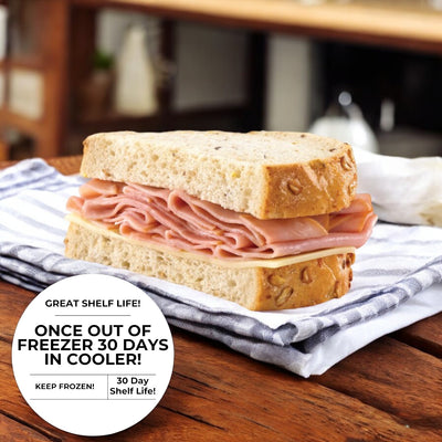 A Ham & Swiss On Rustic Oat Topped Wheat Bread sandwich by E.A. Sween is placed on a cloth napkin. Text reads: "Great shelf life! Once out of the freezer, 30 days in cooler! Keep frozen! 30-day shelf life!