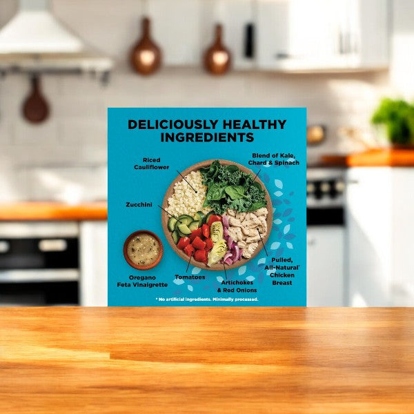 On a kitchen counter, a product display features a bowl of salad with various ingredients like riced cauliflower and pulled chicken. A small container of dressing accompanies the bowl. Text on the display promotes the vegetables and pulled chicken, highlighting it as one of Healthy Choice's Power Bowls: Greek-Style Chicken with Riced Cauliflower, 9.5 oz.