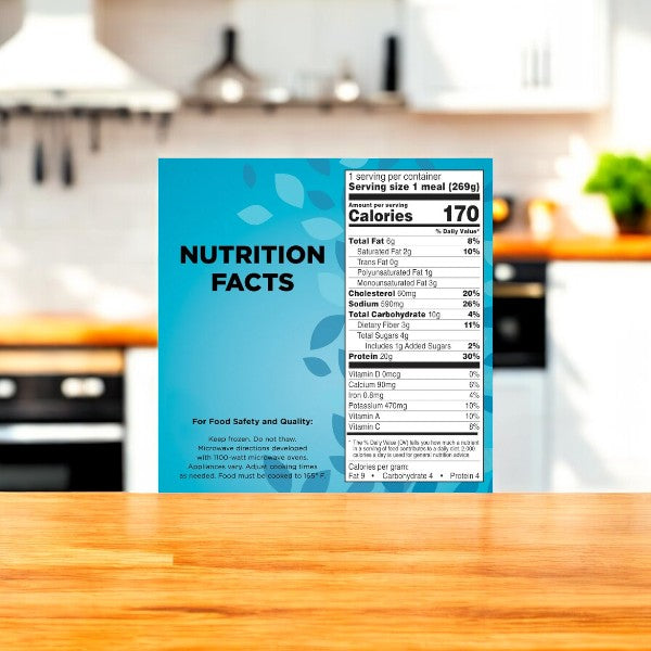 Close-up of a nutritional information label for Healthy Choice Power Bowls Greek-Style Chicken With Riced Cauliflower, 9.5 oz., on a blue background, placed on a wooden surface in a kitchen setting.