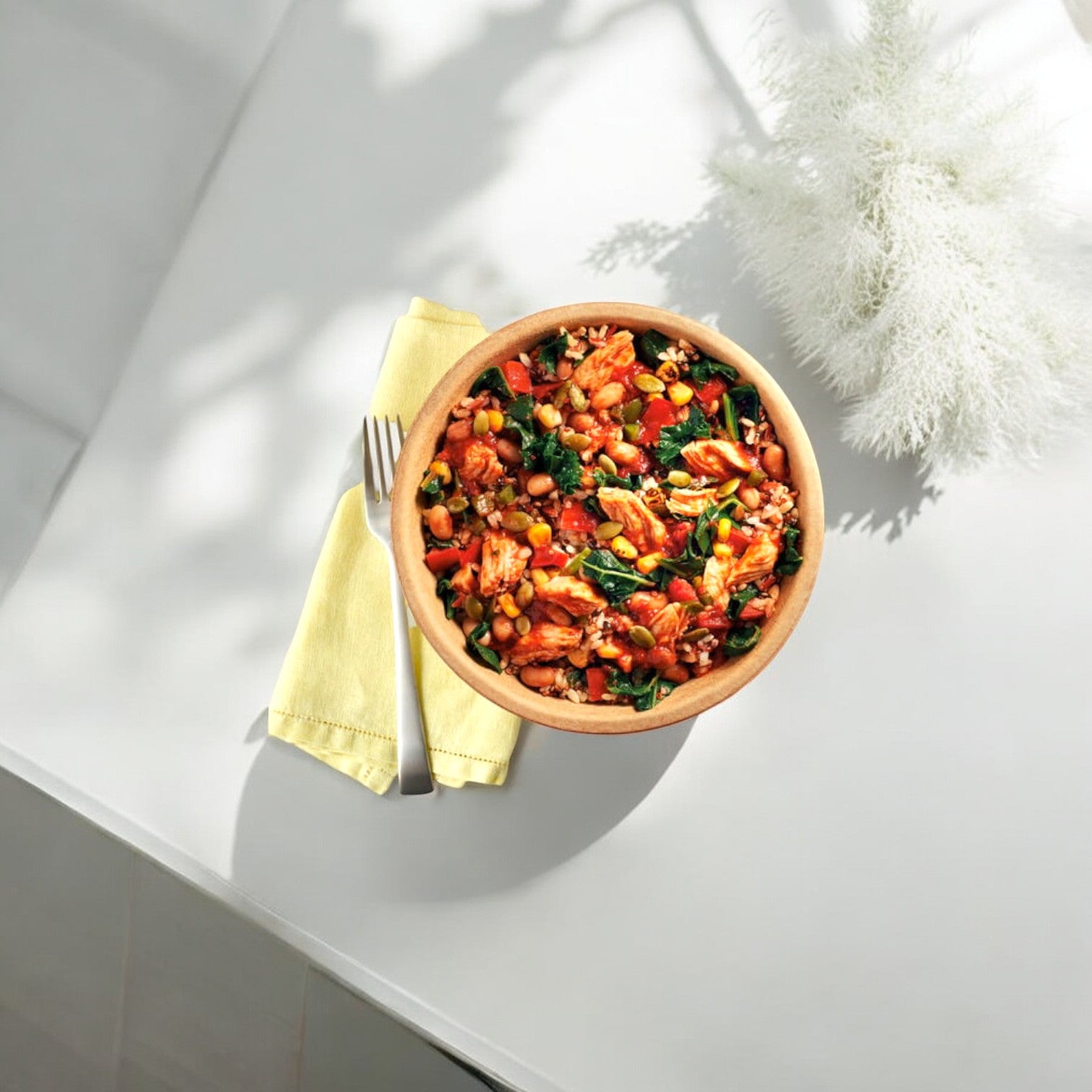 The Healthy Choice Power Bowls Chicken Adobo, a 9.75 oz. serving featuring a nutritious mix of vegetables and grains, is placed on a white surface with a yellow napkin and fork beside it.