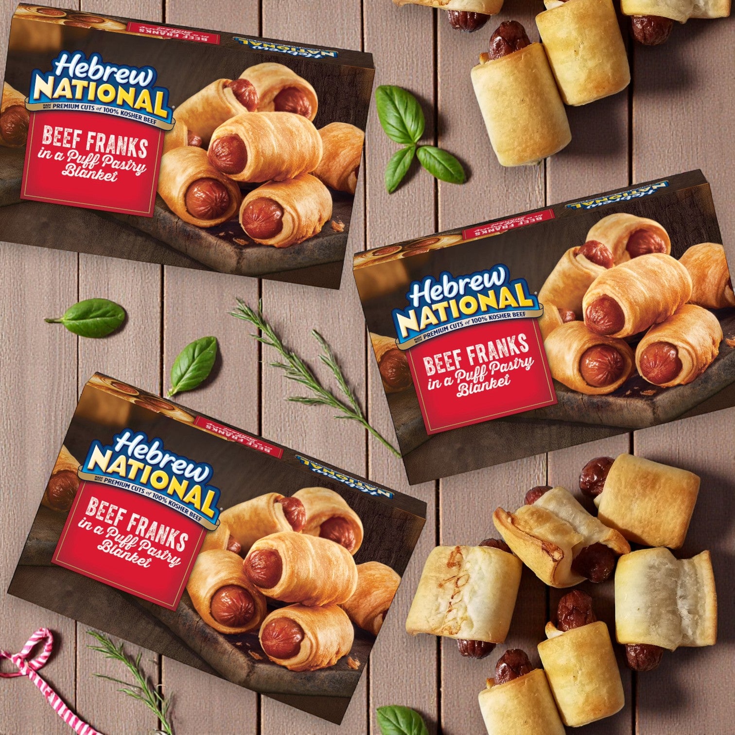 Three 18.4oz boxes of Hebrew National Beef Franks in a Puff Pastry Blanket (3 count each) are shown, with some franks arranged on a wooden surface alongside herbs and skewers.