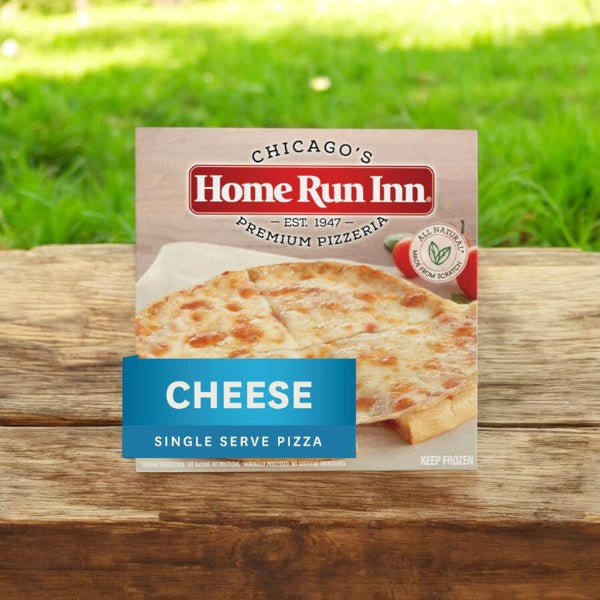 A box labeled "Home Run Inn, Chicago's Premium Pizzeria" sits on a wooden surface, featuring an image of a cheese pizza with buttery flaky crust and real mozzarella cheese, promoting the "Mini Personal Classic Frozen Cheese Pizza.