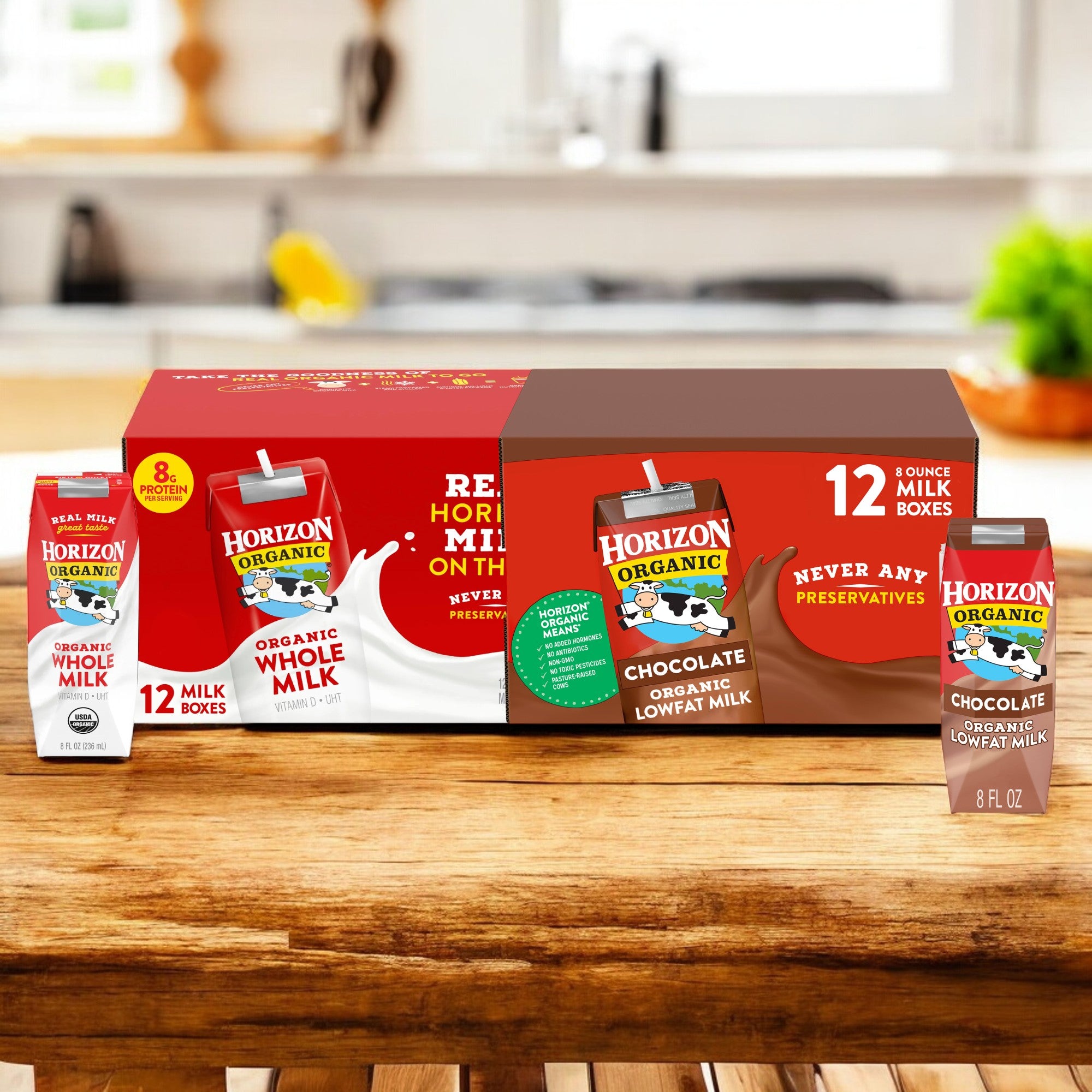 Three cartons of Easy Lunches' Organic Horizon Whole Milk & Chocolate Milk Bundle, featuring whole milk and chocolate lowfat milk, are displayed on a wooden surface with two larger boxed packages in the background.