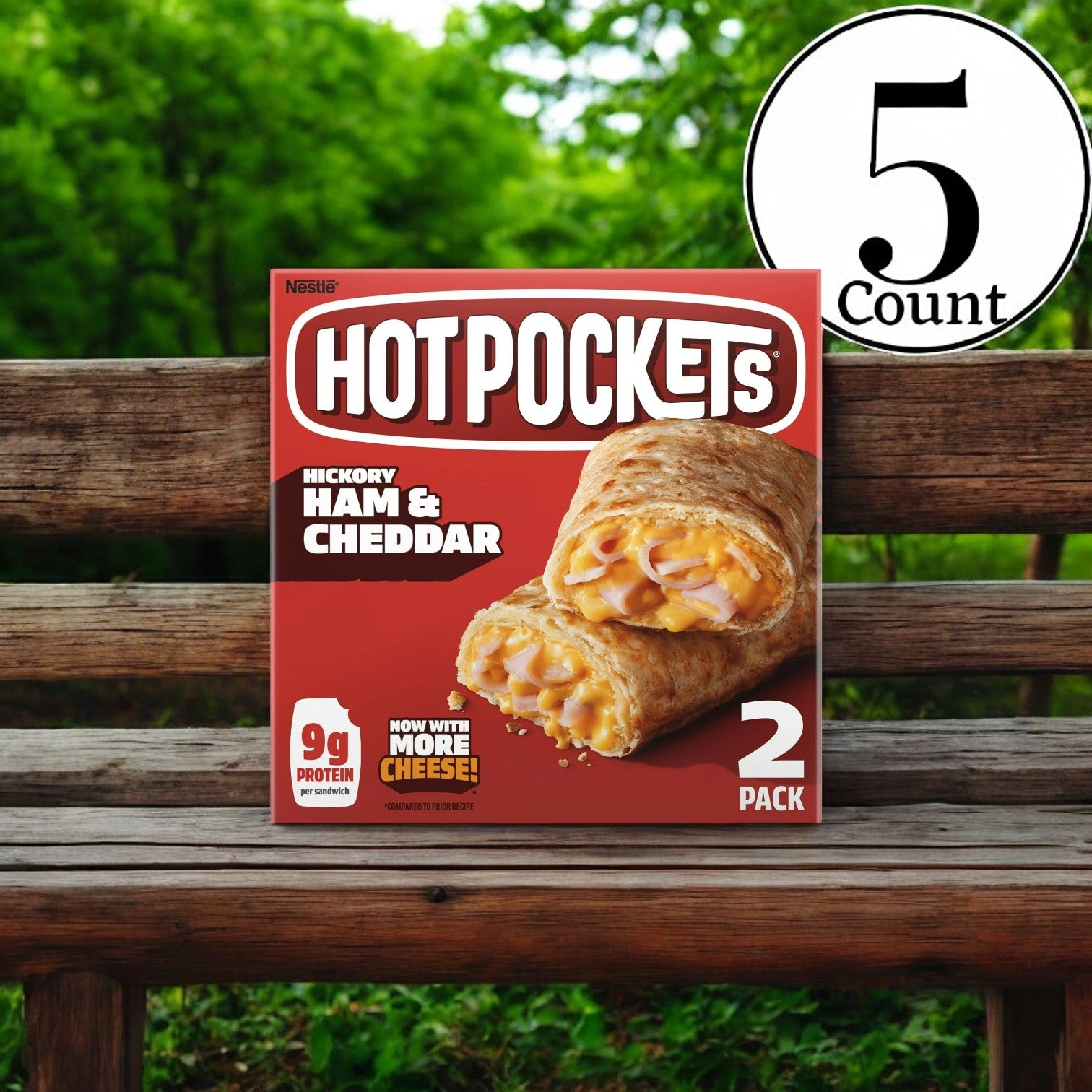 A box of Stouffer's Hot Pockets Frozen Snacks, Ham and Cheddar Croissant Crust, containing two sandwiches per pack in a 5-count package, rests on a wooden bench against a lush green scenery. Ideal for quick and easy meals, each pack guarantees savory satisfaction with every bite.