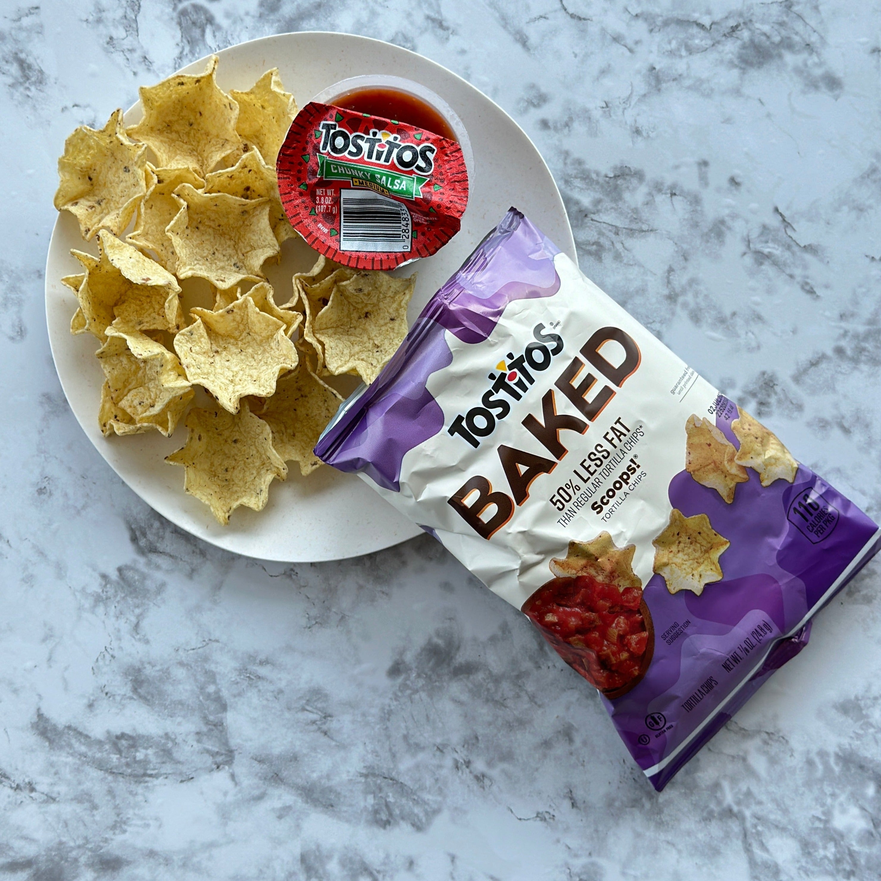 A plate of Tostitos Baked Scoop with Tostitos Chunky Salsa on a marble surface offers the perfect snacking experience.