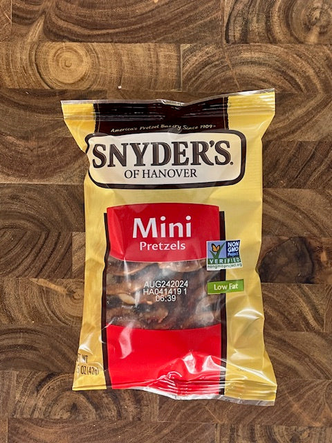 A 1.5 oz. bag of Snyder's of Hanover Mini Pretzels, branded by Snyder's and featuring a Non-GMO Project Verified label along with a low-fat designation and natural ingredients, is placed on a wooden surface.