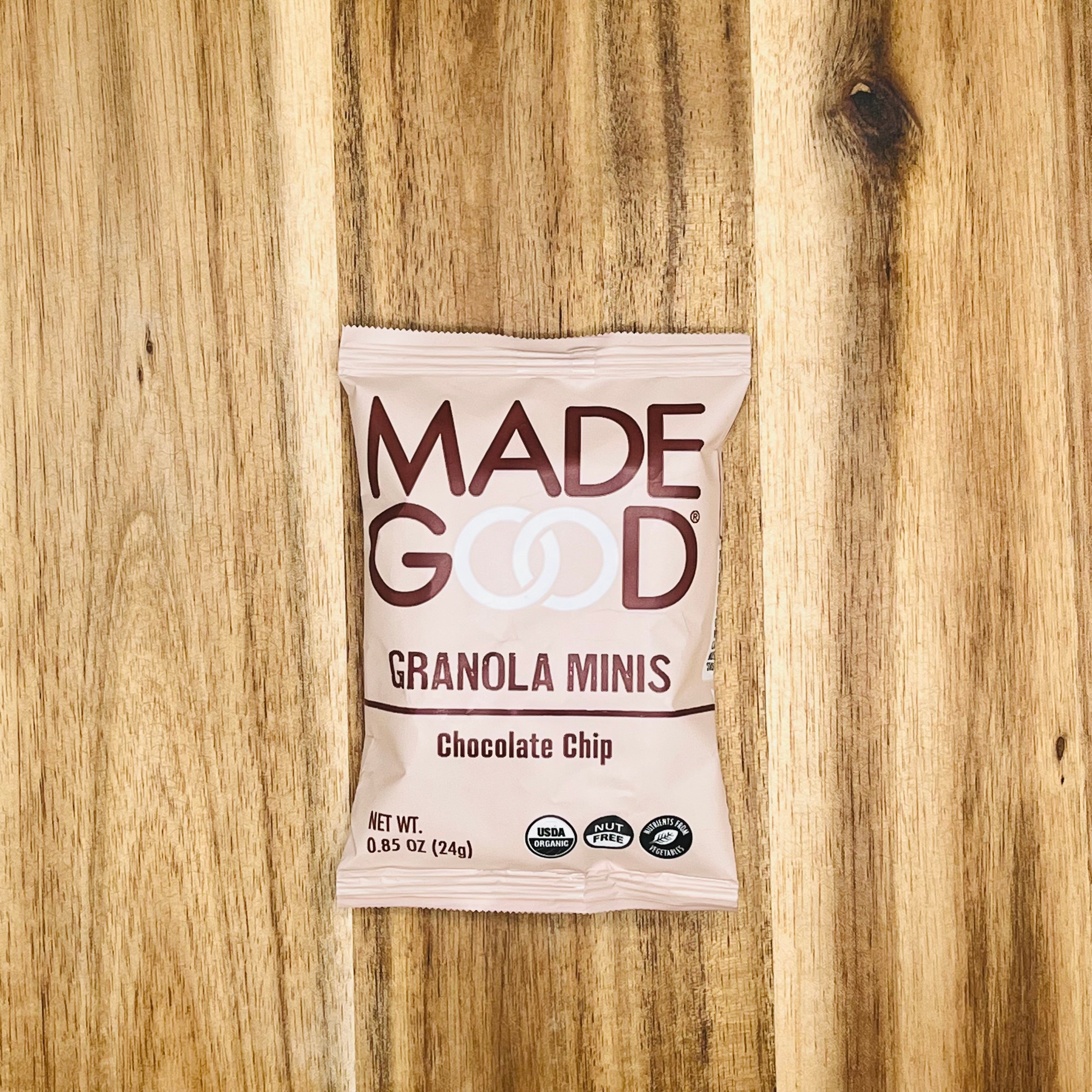 A single 0.85 oz (24g) bag of MadeGood Chocolate Chip Granola Minis, resting on a wooden surface, proudly showcases its organic ingredients, gluten-free oats, and chocolate chips for a delightful snack.