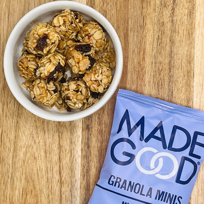 A bowl of madegood granola minis, a nutrient-rich snack, next to a partially visible package labeled "MadeGood Organic Gluten Free Granola Minis Mixed Berry" on a wooden surface.