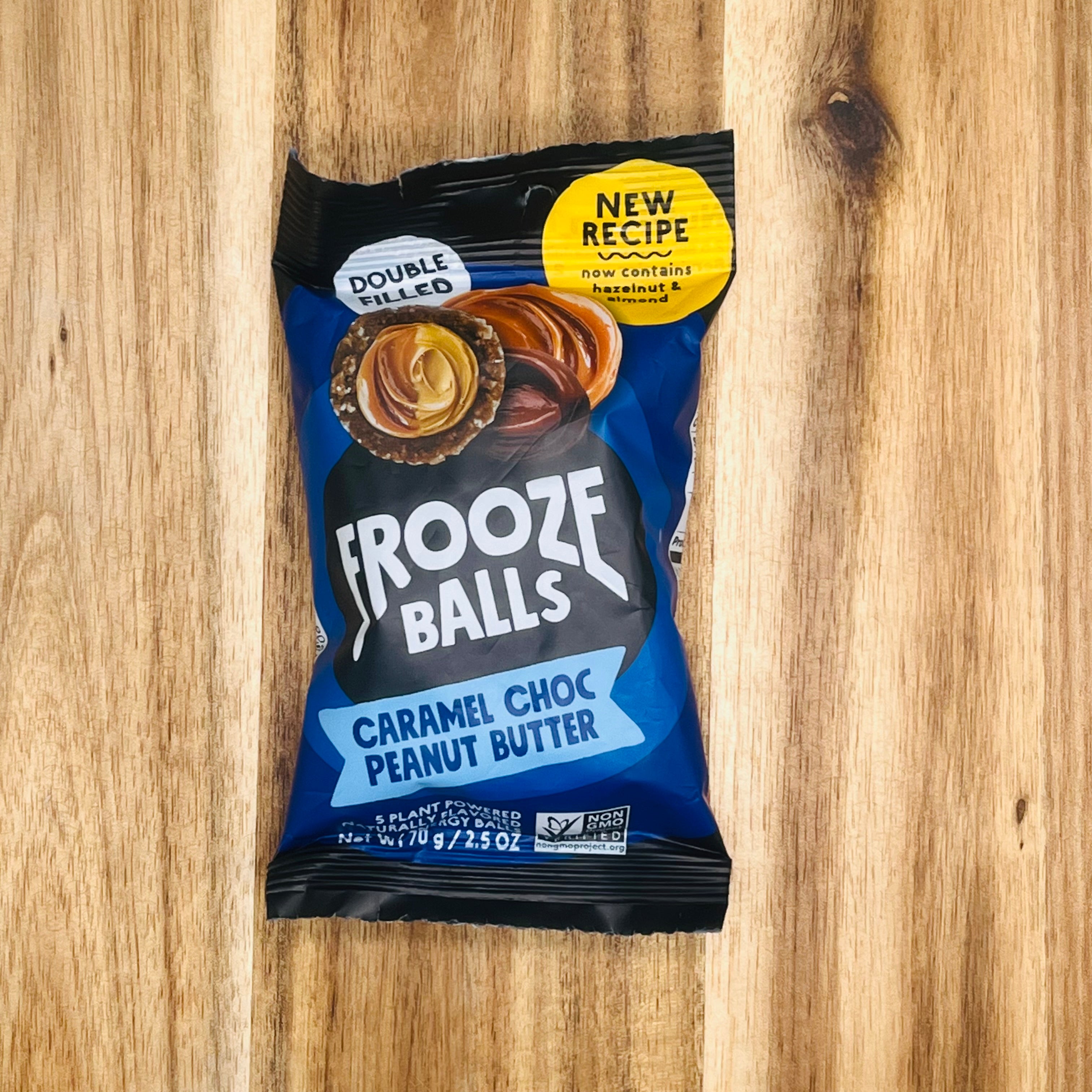 A package of Frooze Balls Chocolate Caramel Peanut Butter - Double-Filled Energy Balls (2.5 oz, 1 Count), boasting a rich chocolatey coating and proudly gluten-free, placed on a wooden surface.