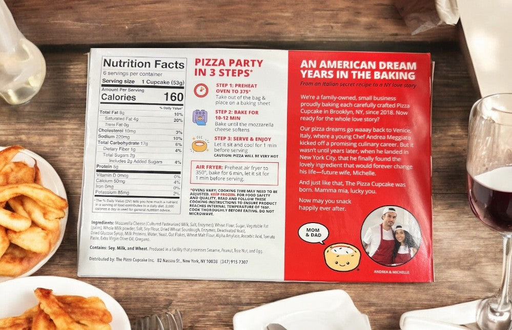 A table with The Pizza Cupcake Margherita, a wine glass, and packaging displaying nutrition facts. The package tells the story and prep steps of these appetizers, including a family photo.