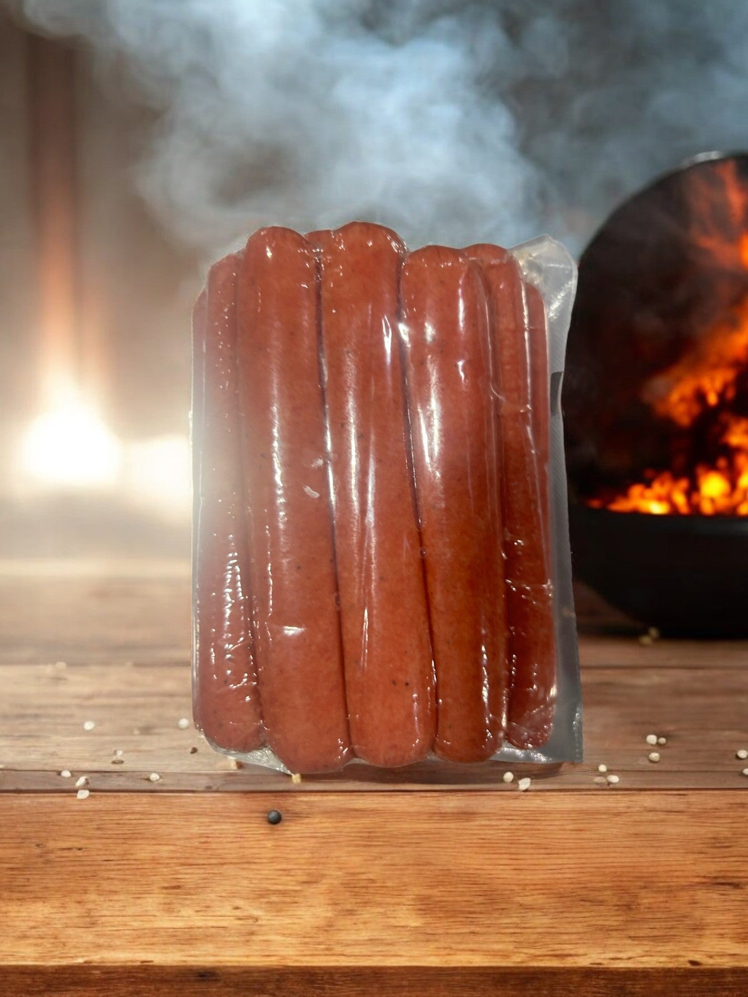 A wooden table holds a vacuum-sealed pack of Vienna Beef Polish Sausage-32 Oz, with a smoky grill and fire visible in the background.