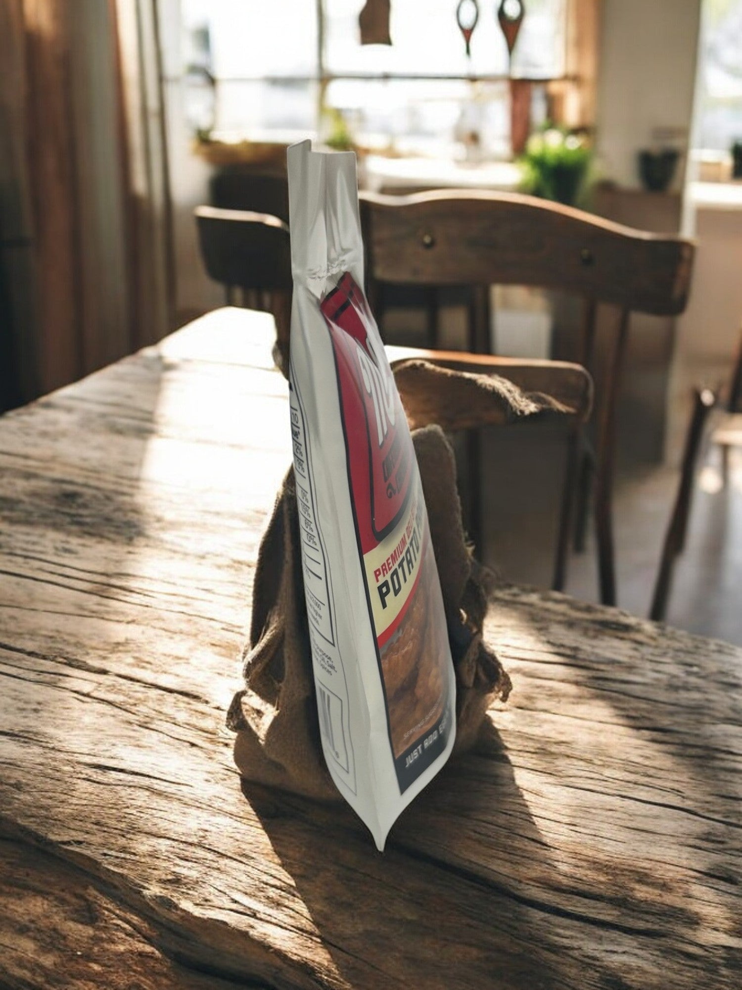 A bag of Manny's Potato Pancake Mix-3 Count sits on a rustic wooden table in a sunlit room, suggesting a cozy gathering. The inviting aroma of homemade potato pancakes drifts through the air, where eager guests await in nearby chairs.