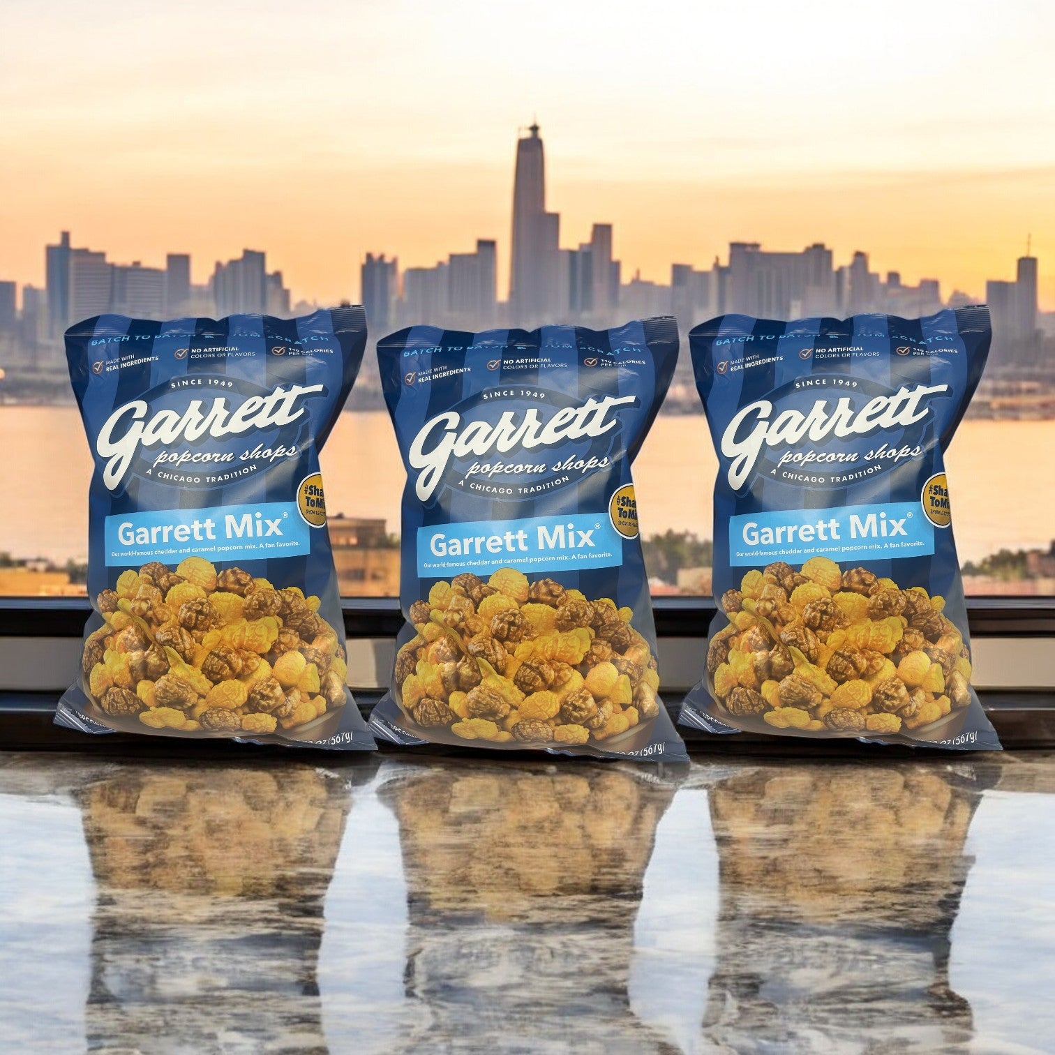 Three bags of Garrett Popcorn Cheddar and Caramel Garrett Mix Popcorn from Garrett are artfully displayed on a reflective surface, with a city skyline in the background, capturing the essence of Garrett Popcorn Shops.