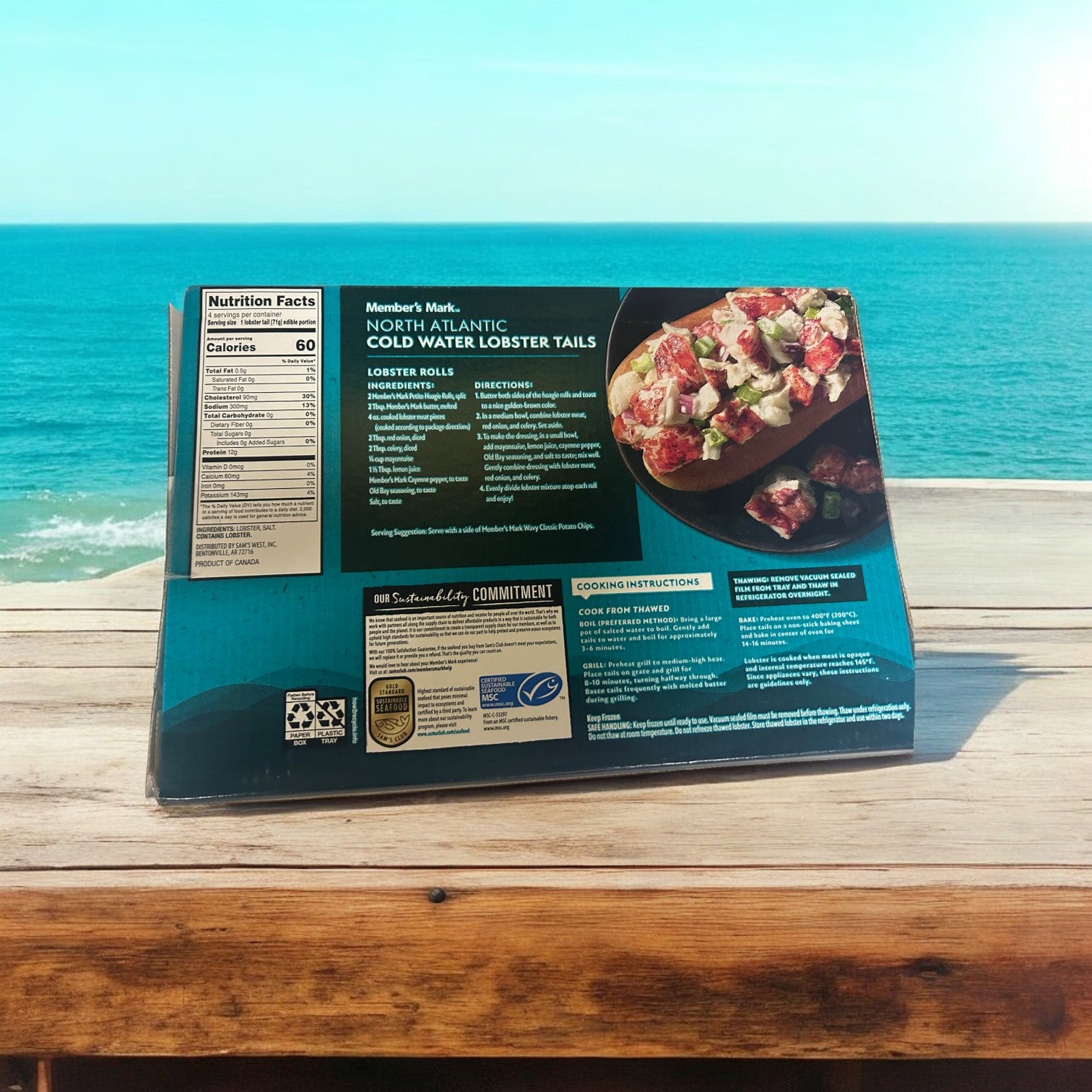 A box of Easy Lunches Member's Mark Cold Water Lobster Tails, Frozen, 4 Count, 3 Packs sits on a wooden table with an ocean view in the background.