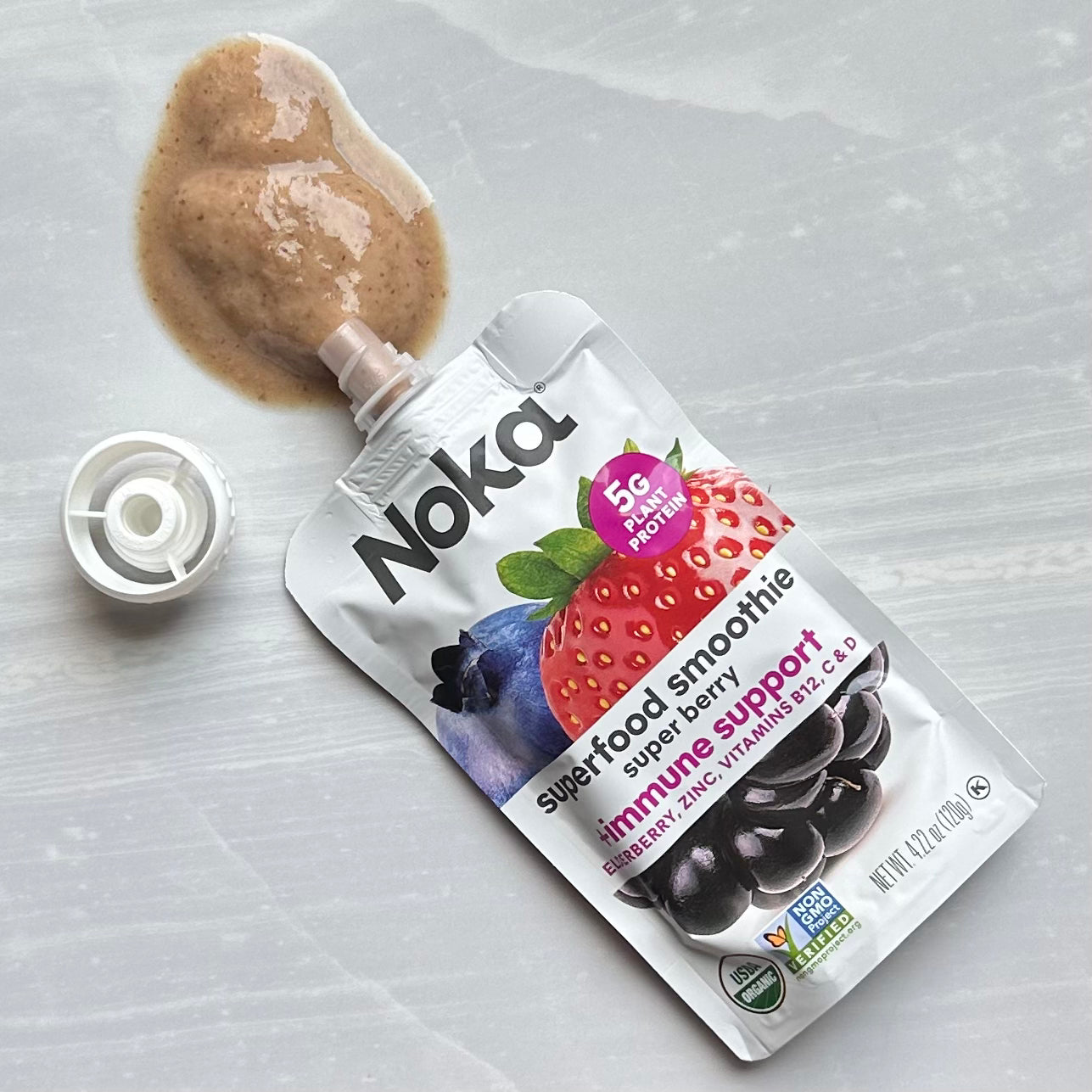 A spilled Noka Organic Super Berry with Plant Protein packet, with the cap removed, showcases organic superfoods like strawberries, blueberries, and dark berries. Advertising 5g of plant protein and immune-boosting support, this on-the-go option from Noka is perfect for a quick and nutritious snack.