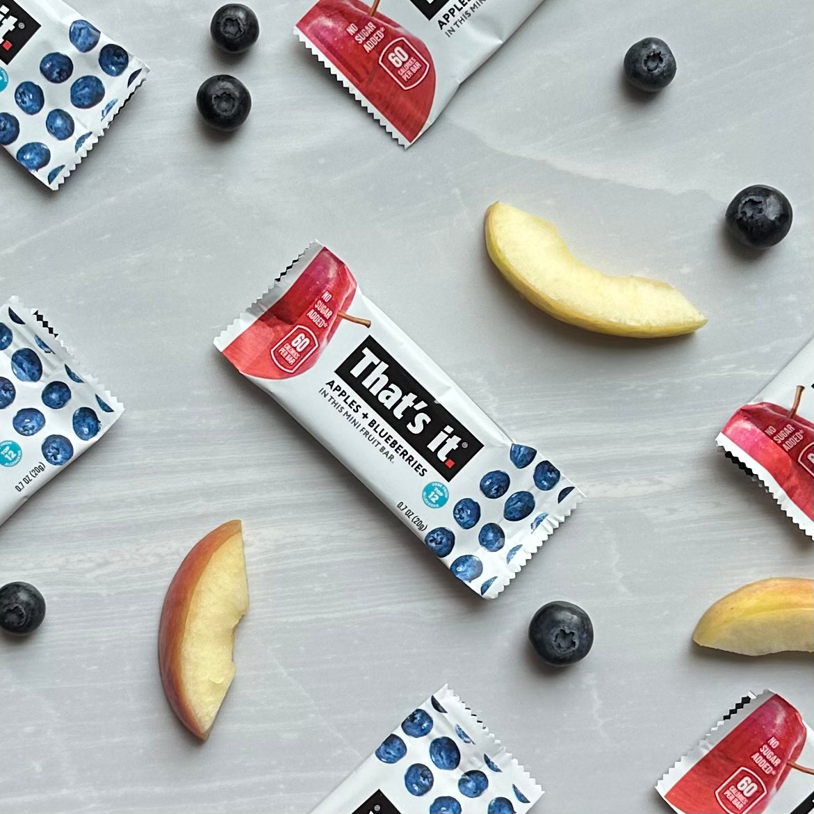 An arrangement of That's It. Gluten-Free Soft & Chewy Blueberry Mini's Ready-to-Eat Fruit Bars, fresh apple slices, and blueberries on a light gray surface.