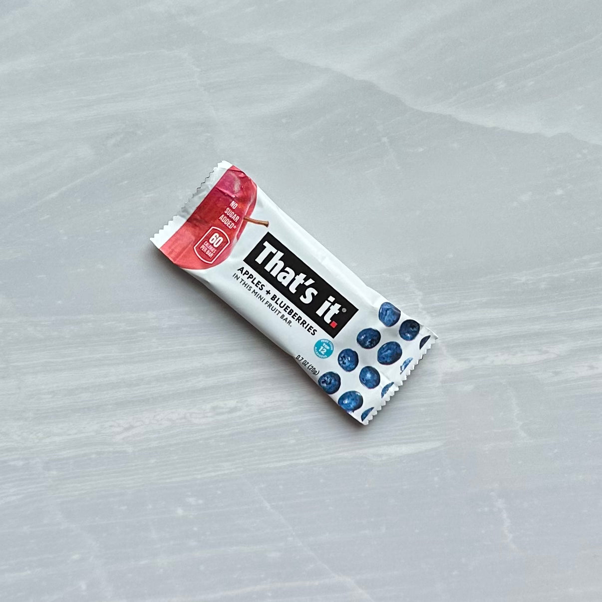 A That's it. Gluten-Free Soft & Chewy Blueberry Mini's Ready-to-Eat Fruit Bar on a gray surface, labeled with "Apples + Blueberries" and 80 calories per bar; these all-natural fruit snack bars are made in an allergen-free facility.