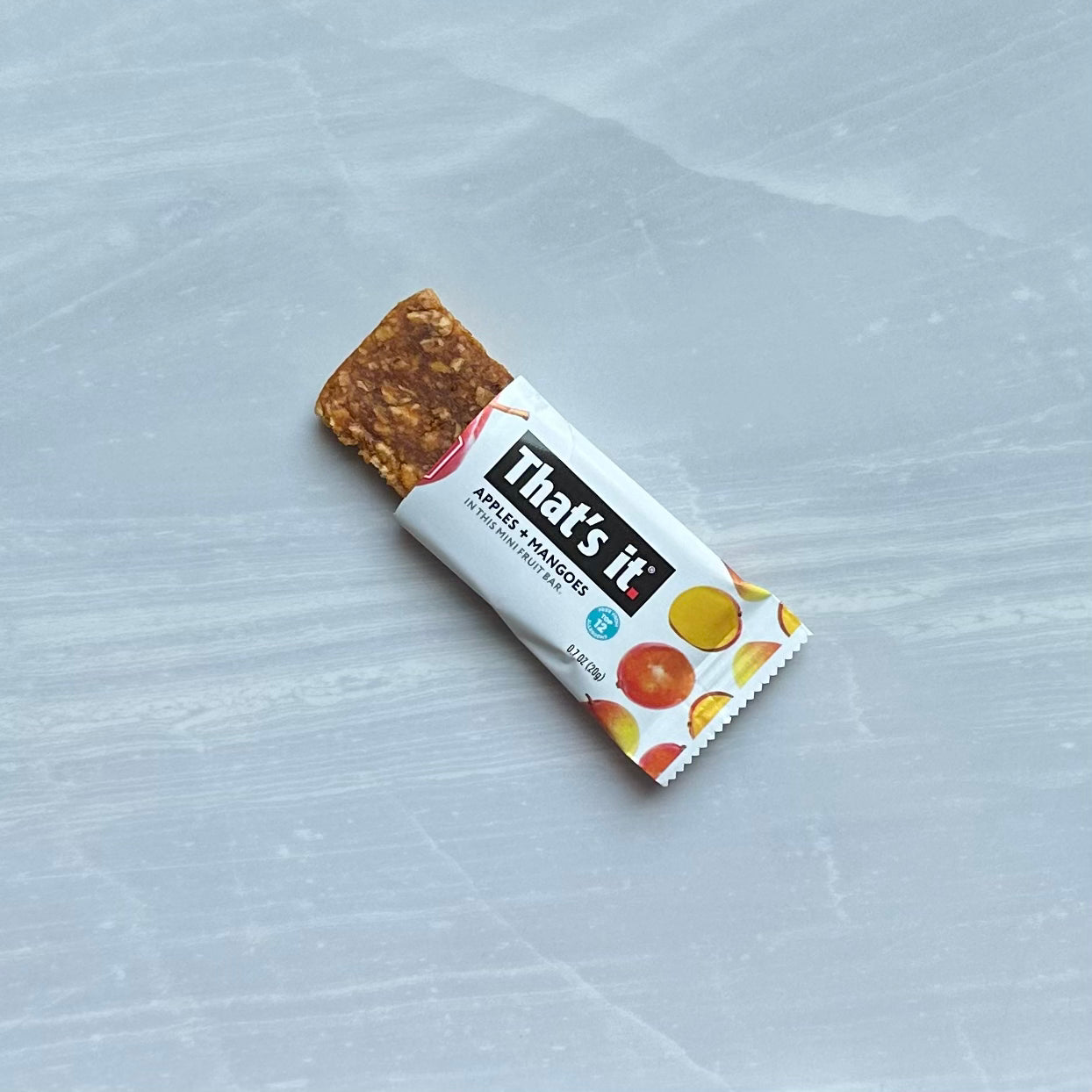 A soft and chewy mango mini fruit bar in partially open packaging labeled "That's it. Gluten-Free Soft & Chewy Mango Mini Fruit Bars" on a gray marble surface, showcasing an all-natural fruit snack that's vegan, gluten-free, and dairy-free.