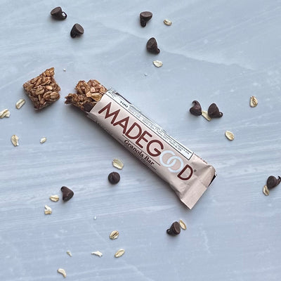 A partially opened MadeGood Mixed Berry Granola Bar on a marble surface with chocolate chips and gluten-free oats scattered around, perfect for those seeking vegan snacks.