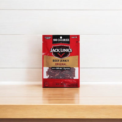 A 1.25 oz package of Jack Link's- Beef Jerky Original, made from 100% premium beef and labeled with 100 calories, stands on a wooden surface against a plain white background.