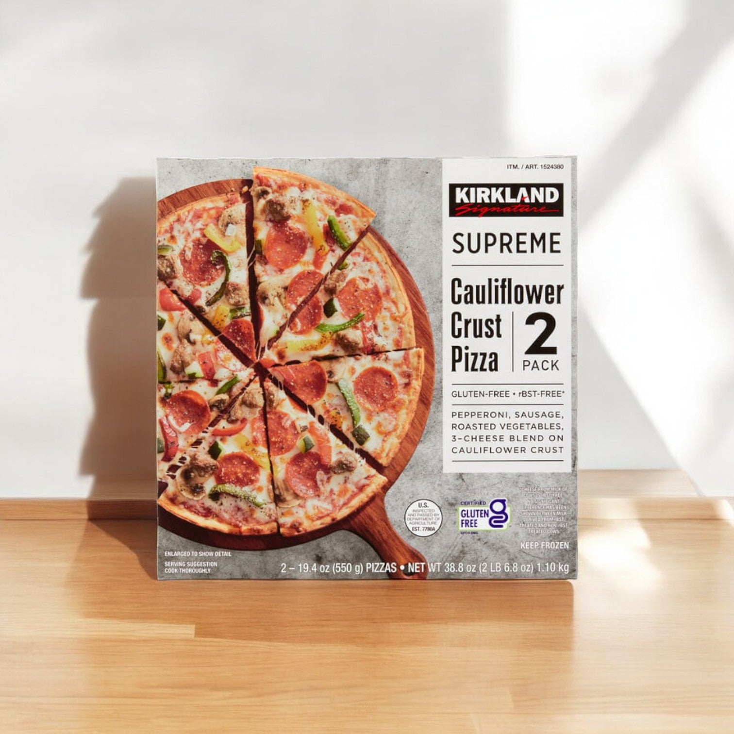 The Kirkland Signature Cauliflower Crust Pizza, Supreme, 2-count -1 Pack, showcasing delicious breakfast ingredients such as hickory smoked bacon, is enticingly displayed on a wooden surface with its shadow enhancing the depth of the scene.