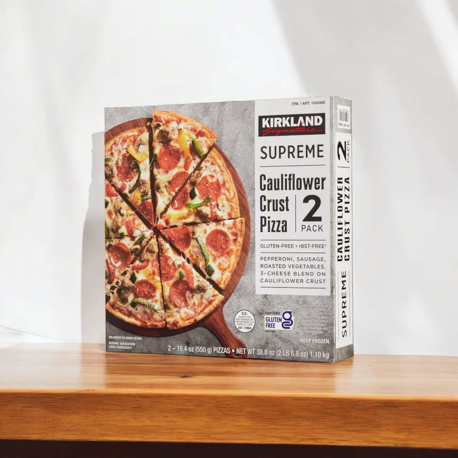 A box of Kirkland Signature Cauliflower Crust Pizza, Supreme - 2-count-3 pack, rests on a wooden surface. The packaging showcases a mouth-watering gluten-free pizza loaded with pepperoni, sausage, vegetables, and cheese. Ideal for those seeking supreme toppings in a convenient multi-pack option.