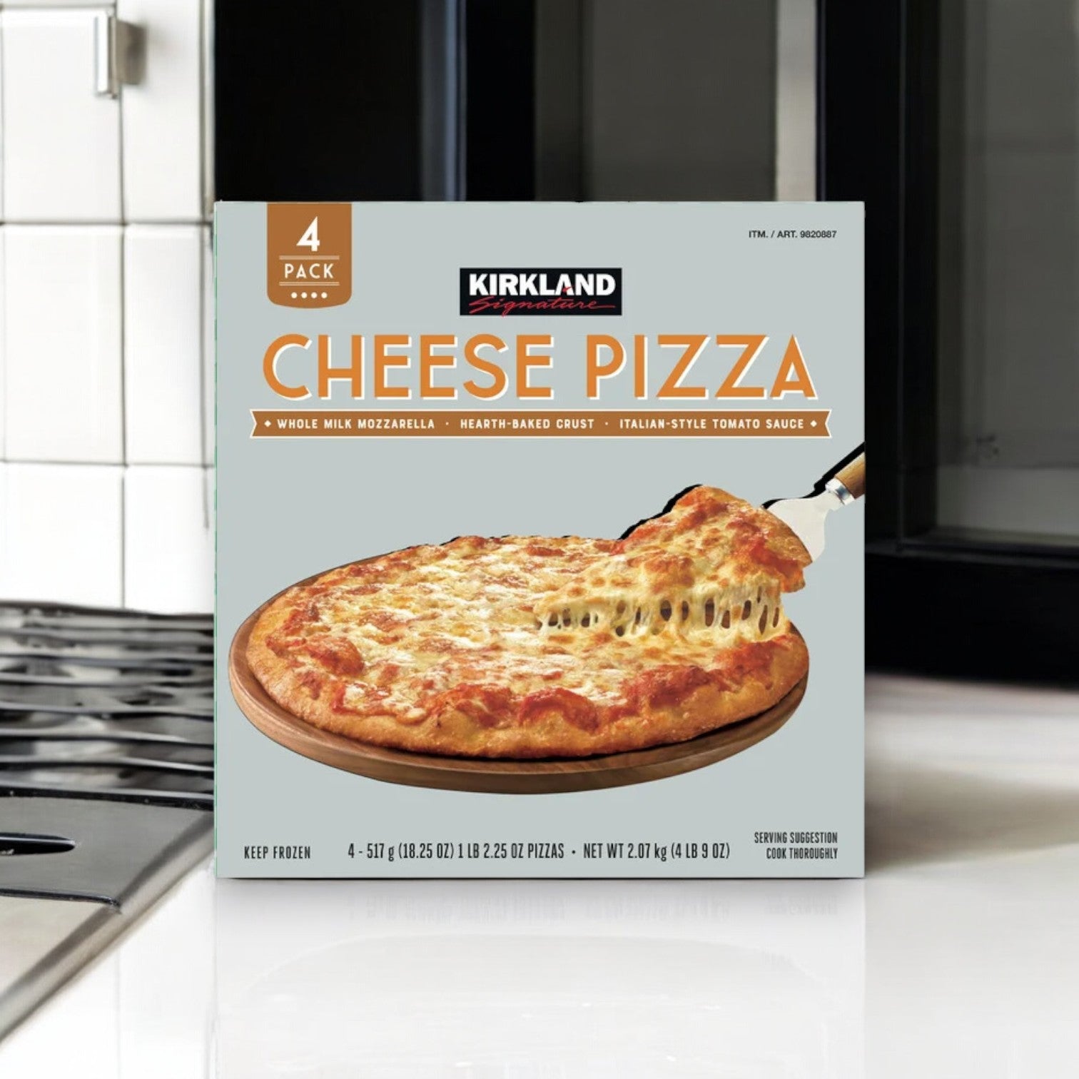 A pack of Kirkland Signature Cheese Pizza, featuring four pizzas with a hand-stretched crust and a premium blend of mozzarella and provolone cheese, is invitingly displayed on the kitchen counter next to the stovetop.