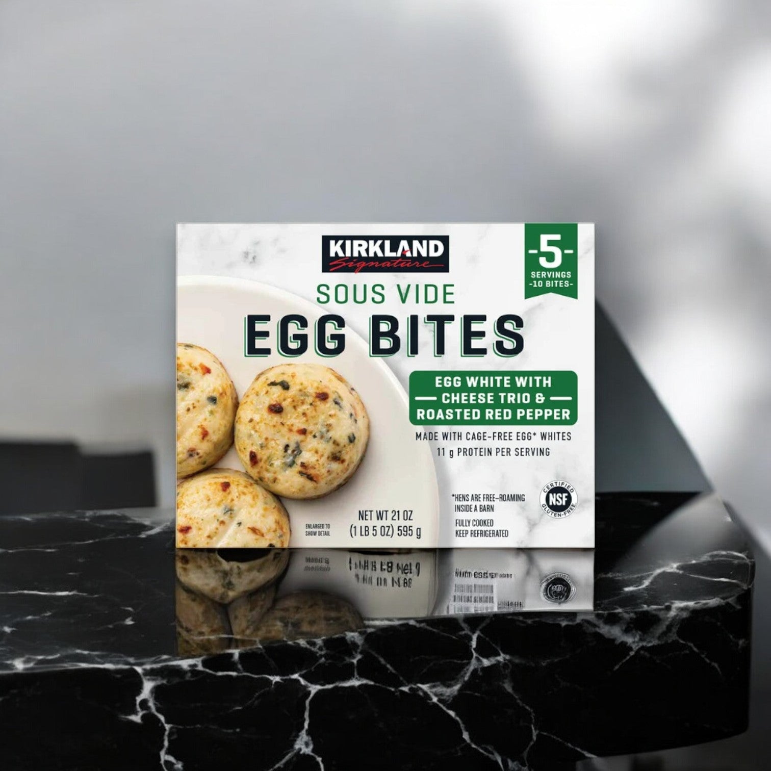 A box of Kirkland Signature Egg White with Cheese Trio and Peppers Egg Bites, in a 10-count pack, is artfully displayed on a dark marble surface.