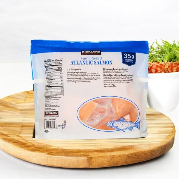 A bag of Kirkland Signature Farmed Atlantic Salmon, center-cut portions weighing 6 oz to 8 oz each and totaling 9 pounds across three bags, rests on a wooden tray. Behind it, nutritional information and a bowl of food add context to this sustainably farm-raised seafood delight, known for its omega-3 fatty acid richness.