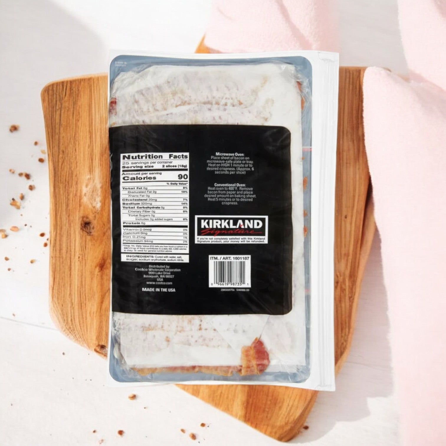 Kirkland Signature Fully-Cooked Bacon, Hickory Wood Smoked rests on a wooden board with its nutrition facts label facing up against a light-colored background. Made to deliver both convenience and flavor, this high-quality bacon comes in 1 lb packs, totaling 3 pounds.