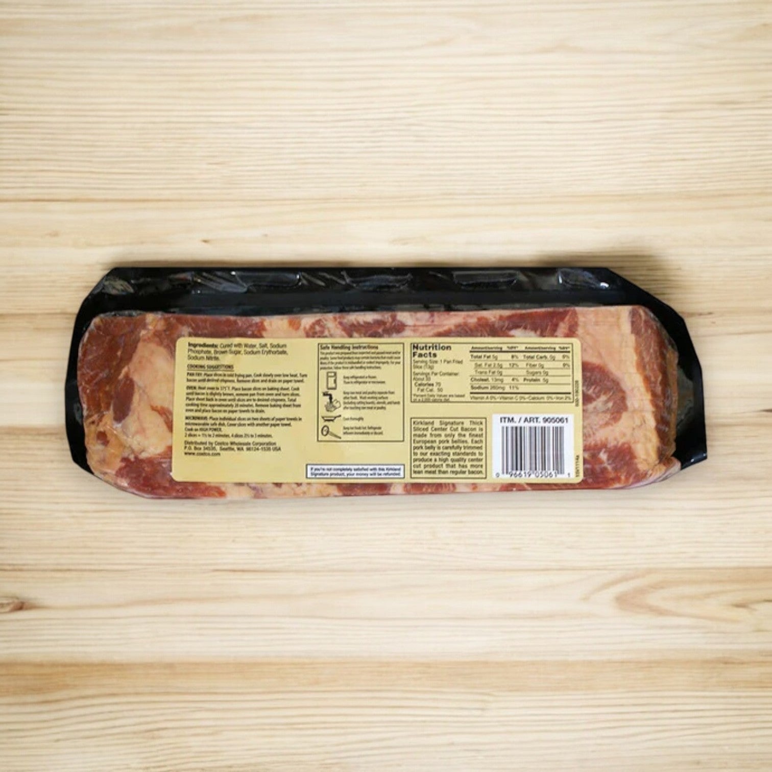 Kirkland Signature Thick Sliced Bacon, 1.5 lbs, 2-count package placed on a wooden surface, viewed from the back showing nutritional information and barcodes.