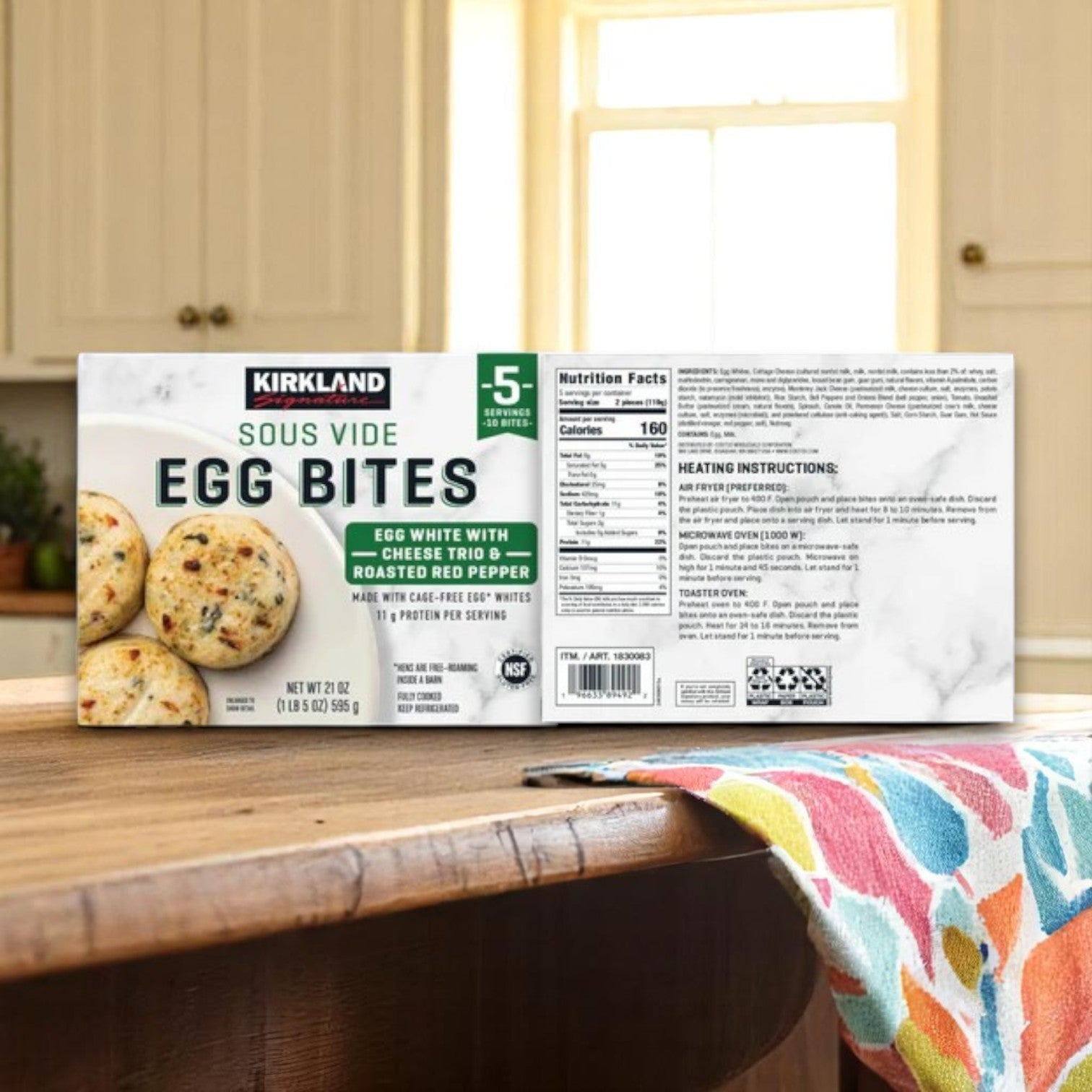 A Kirkland Signature Egg Bite Bundle – 20 Count sits on a wooden kitchen counter, with a colorful towel beside it and a blurred kitchen backdrop.