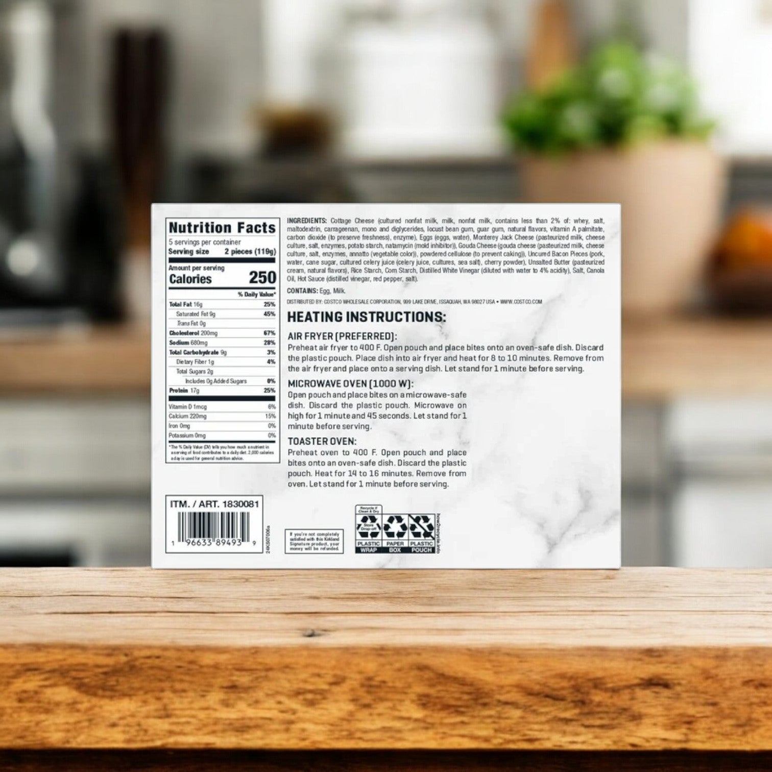 On a wooden countertop, a box of Kirkland Signature Uncured Bacon and Gouda Egg Bites displays the nutrition facts, ingredients, and heating instructions. The softly blurred kitchen background emphasizes the delicious appeal of these Gouda Egg Bites with Uncured Bacon, ready to be savored from one of the three boxes included in this 10-count package.